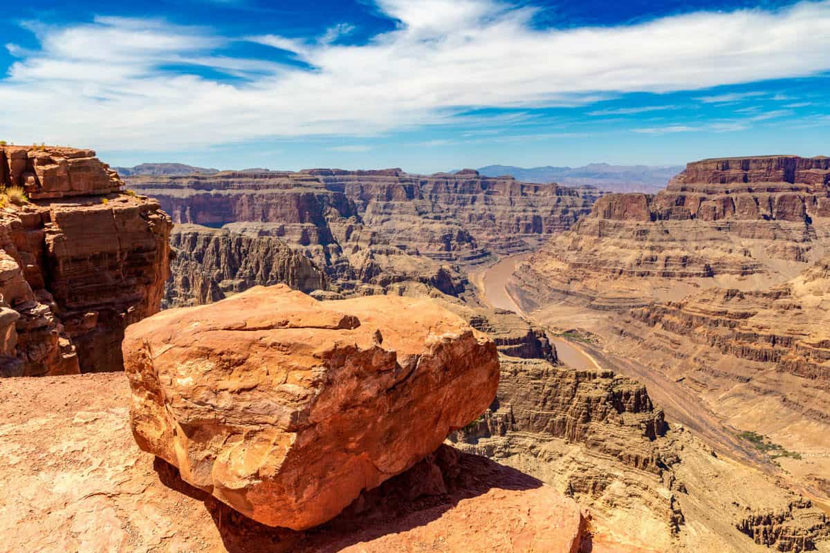 Large ochre boulder on the South Rim of Grand Canyon National Park, with Canyon cliffs visible.