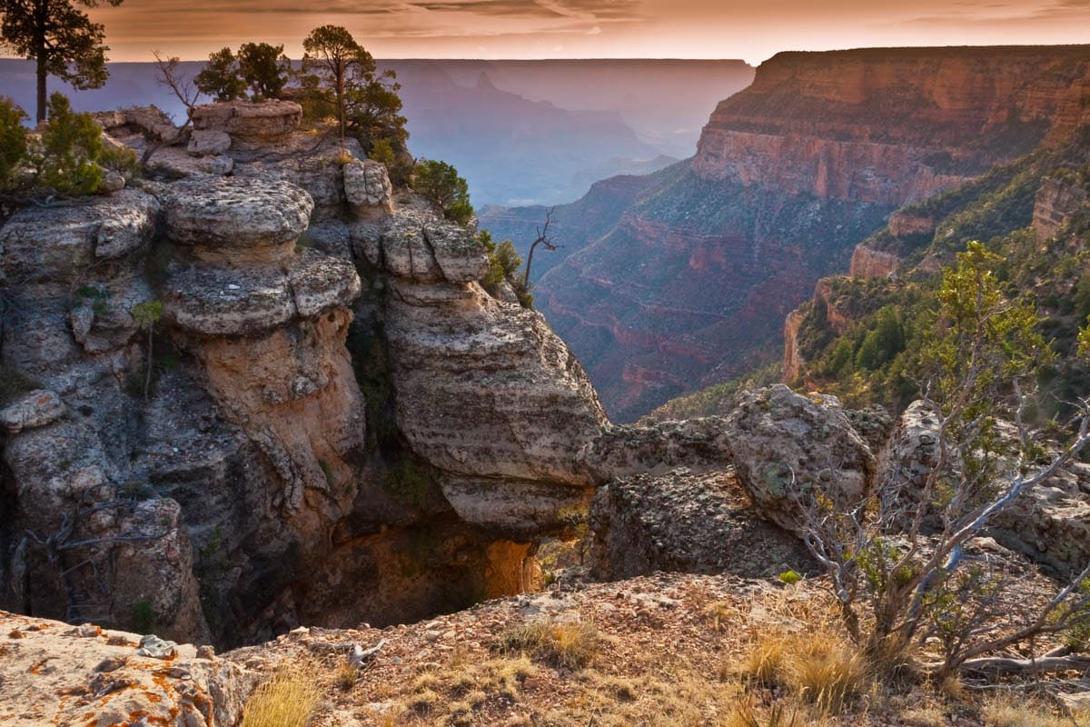 Weathered rock pinnacles beside a deep gorge in Grand Canyon National Park, with Rim shrubs visible.