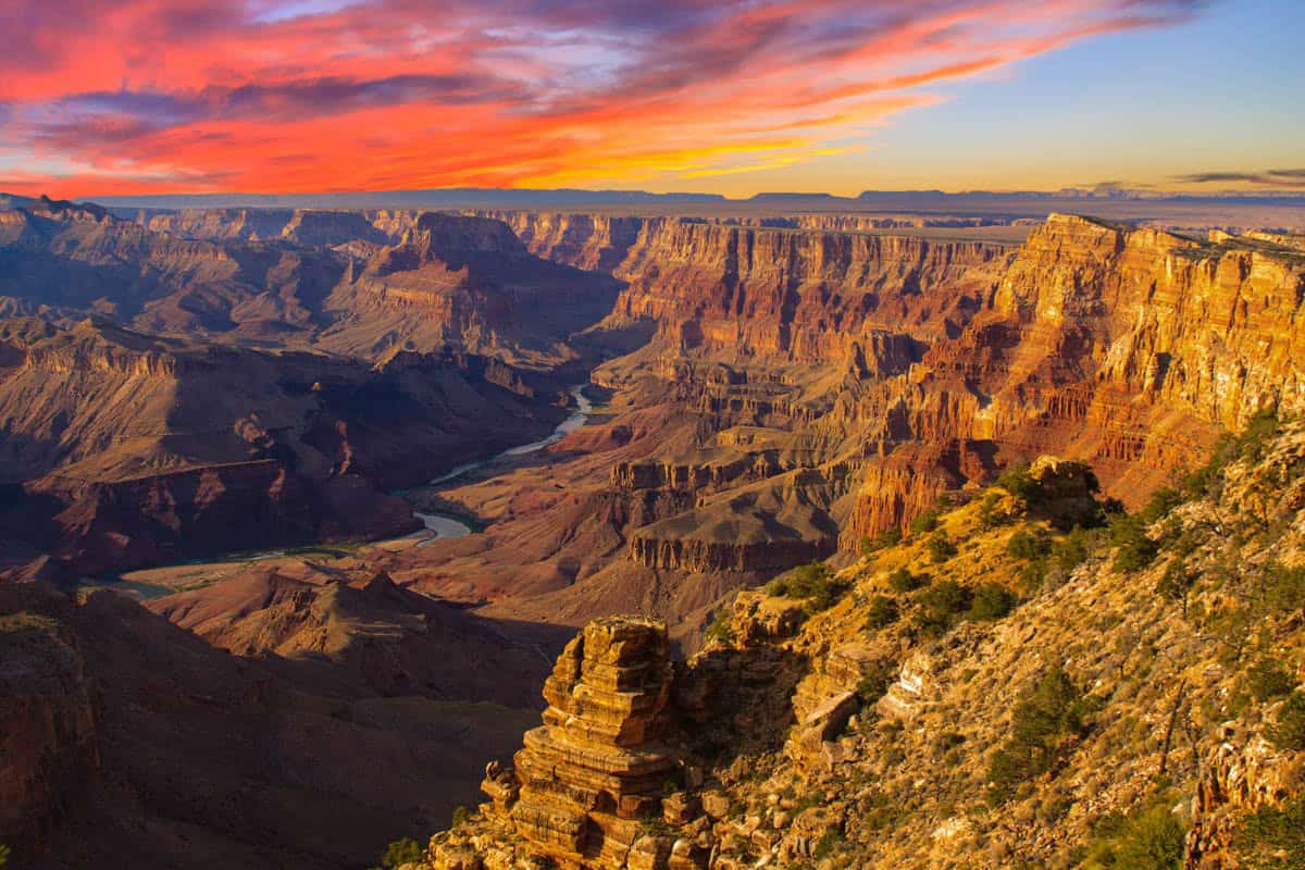 The Colorado River runs below dark cliffs and a fiery sky in Grand Canyon National Park, Arizona, United States.
