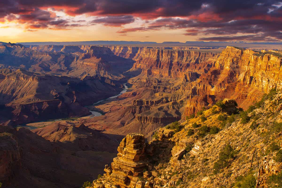 Colorado River winding below sunlit cliffs in Grand Canyon National Park, with Layered canyon walls visible.