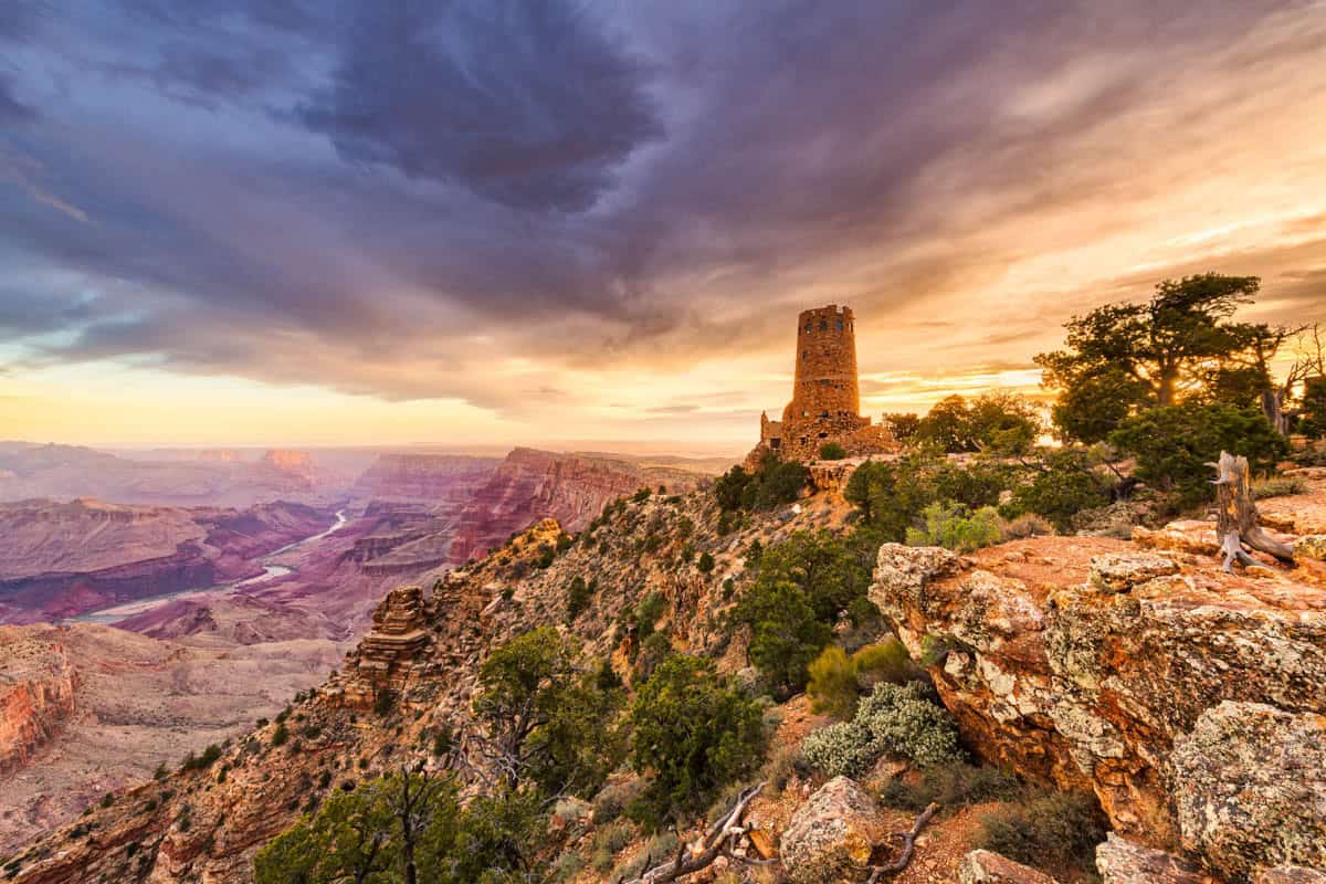 Historic stone watchtower and the Colorado River at sunset beside Juniper trees in Grand Canyon National Park, Arizona, United States.